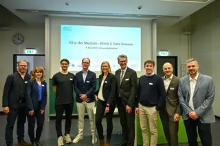Gruppenfoto von Organisations- und Sprecherteam vor der Eröffnungsfolie. Von links nach rechts: Dr. Rainer Borgstedt, Tanja Kirchner, Friedrich Schwarz, Dr. Jan Moritz Middeke, Jun.-Prof. Dr. Carolin Schneider, Thorsten Kaatze, Max Schüler, Prof. Dr. Florian Weißinger, Dr. Enver Aydilek. Nicht im Bild: die Vortragenden Prof. Dr. Wolfram Klapper, Prof. Dr. Philipp Cimiano und Dr. Düsing.